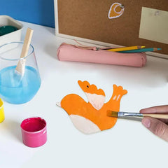 Child painting a cartoon fox with a paintbrush on a white surface.