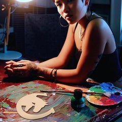 Person sitting at a table with art supplies, including a paint palette and brush.
