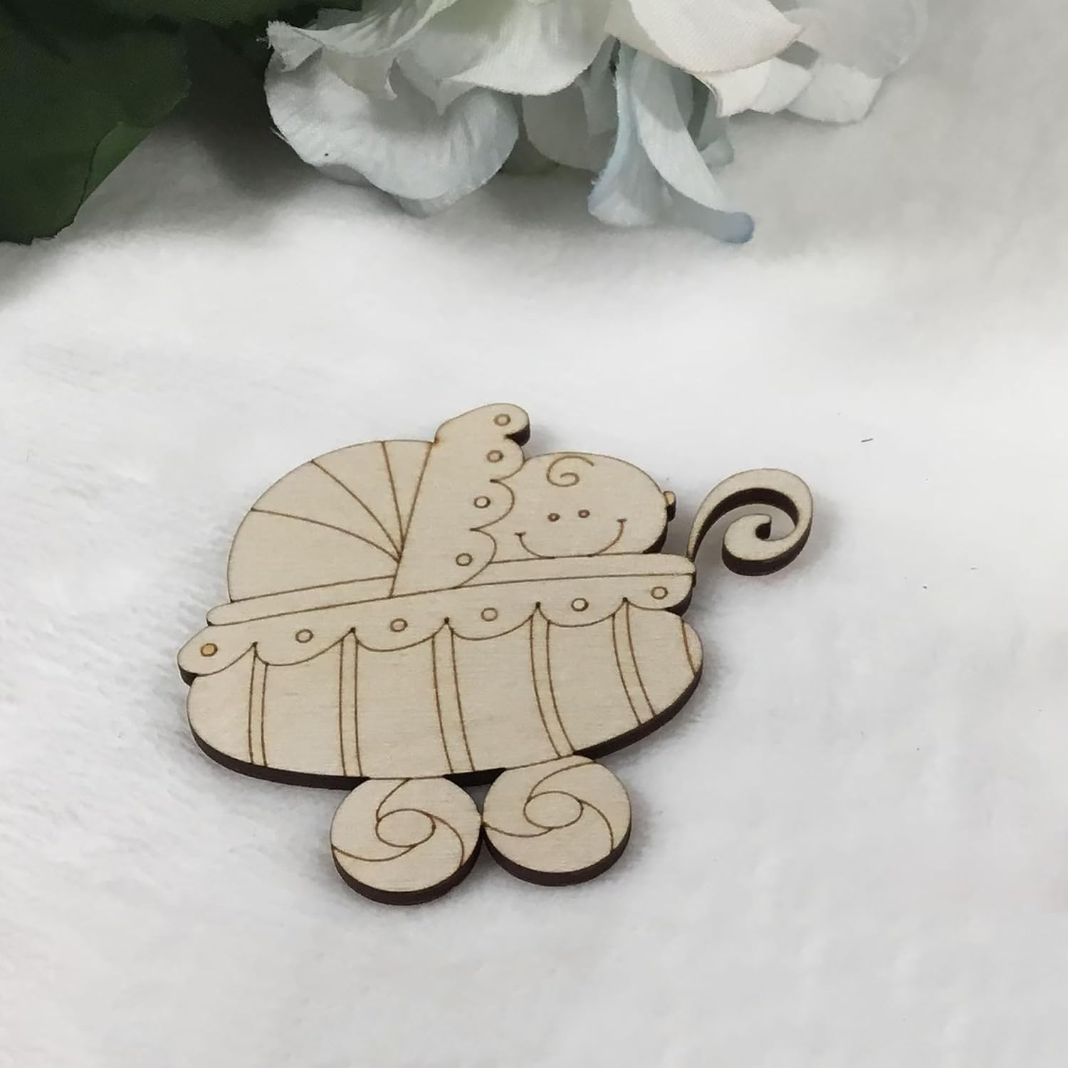 Wooden baby carriage ornament on a white surface with flowers in the background