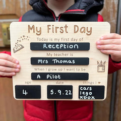 Person holding a wooden sign with 'My First Day of Reception' text and personal details.