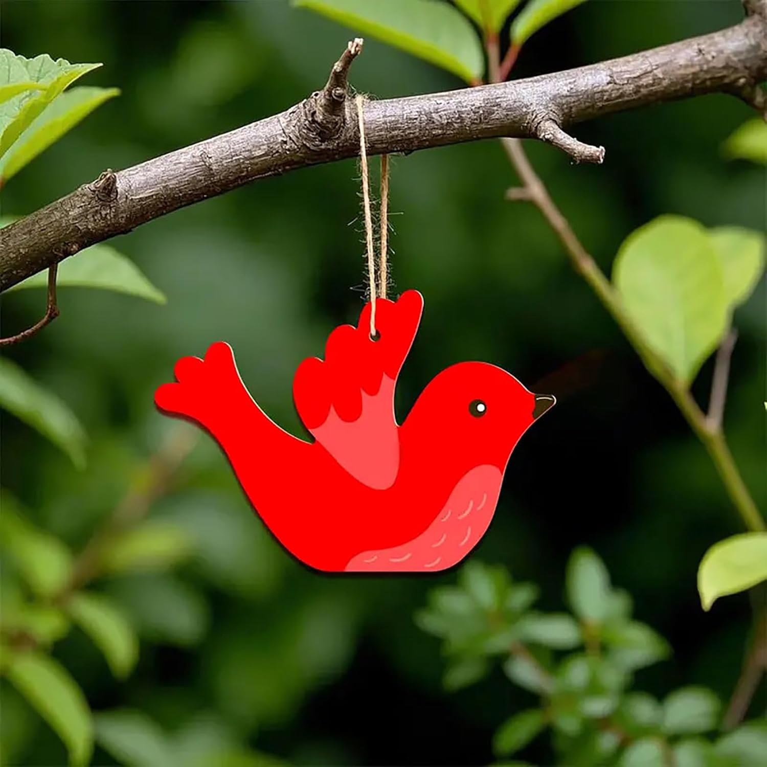 Red bird-shaped ornament hanging from a branch with green leaves in the background