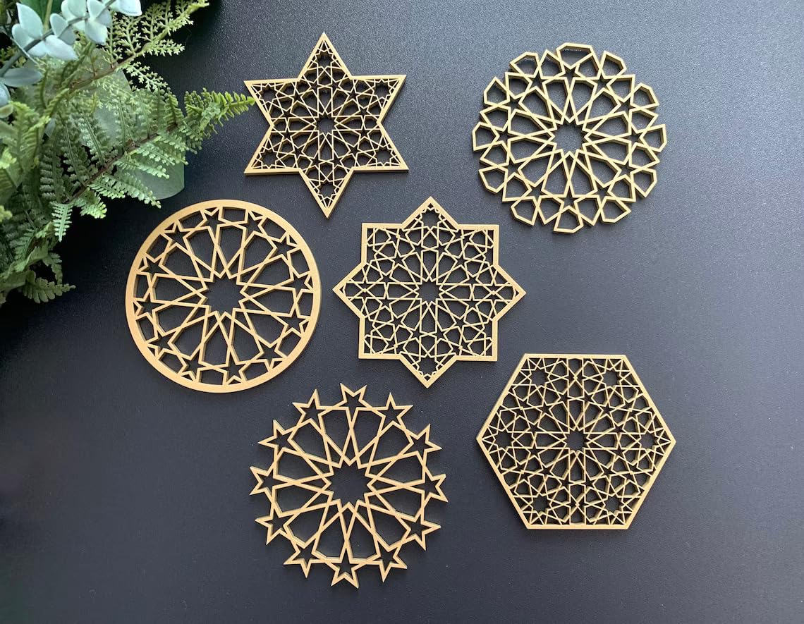 Set of gold geometric coasters on a dark surface with greenery.