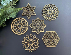 Set of gold geometric coasters on a dark surface with greenery.