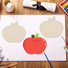 Children's painting of a red apple with two unpainted apple shapes on a white sheet of paper, surrounded by art supplies on a wooden table.