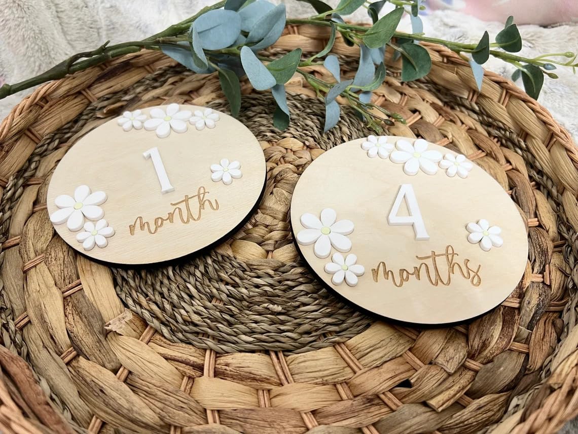 Two wooden discs with '1 month' and '4 months' text on a woven mat with greenery.