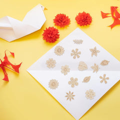 Decorative gold stencils on a white sheet with red flowers and paper birds on a yellow background