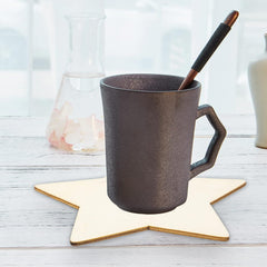 Dark gray mug with a wooden spoon on a star-shaped coaster on a light wooden surface.