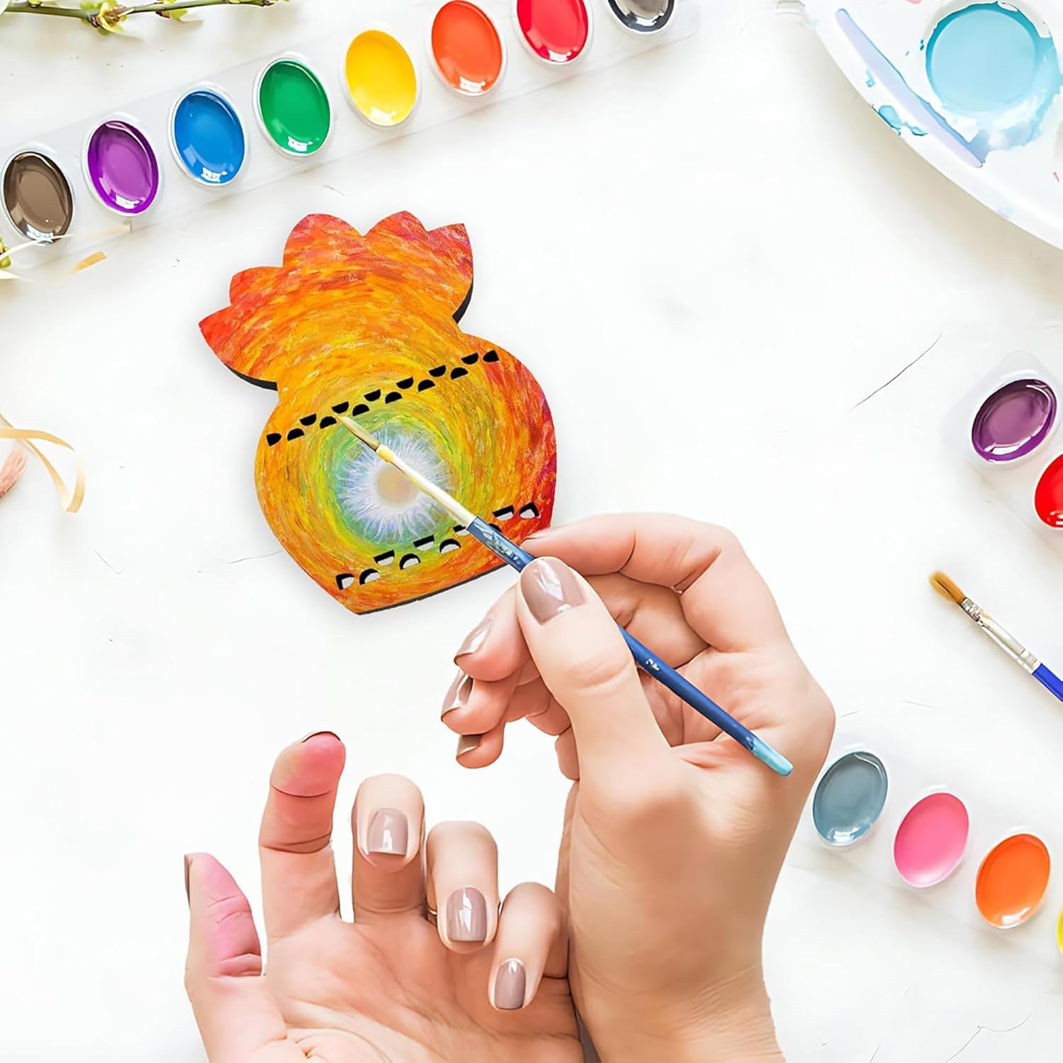Person painting a colorful pineapple-shaped object with watercolors on a white surface.