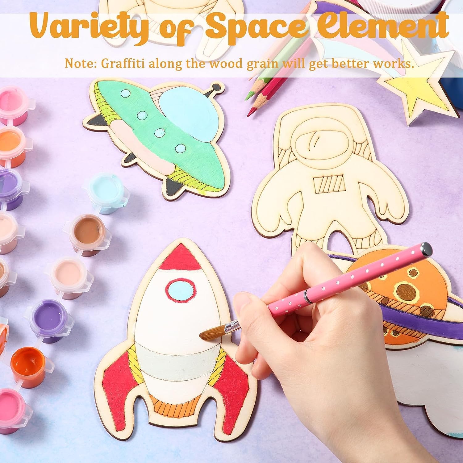 Coloring wooden space-themed shapes with paint and a brush on a light purple background.
