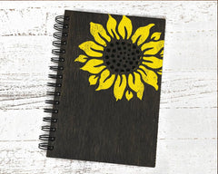 Black notebook with a yellow sunflower design on a white wooden surface