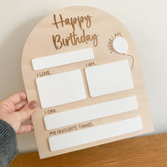 Wooden birthday questionnaire board held by a hand on a wooden surface.