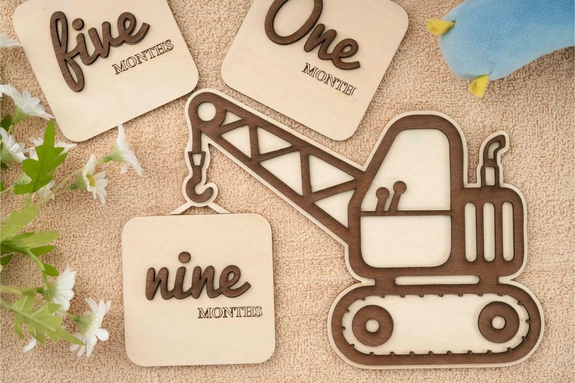 Wooden excavator-shaped milestone with 'nine months' text on a textured surface with flowers.