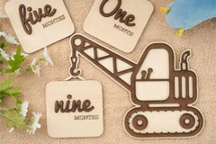 Wooden excavator-shaped milestone with 'nine months' text on a textured surface with flowers.