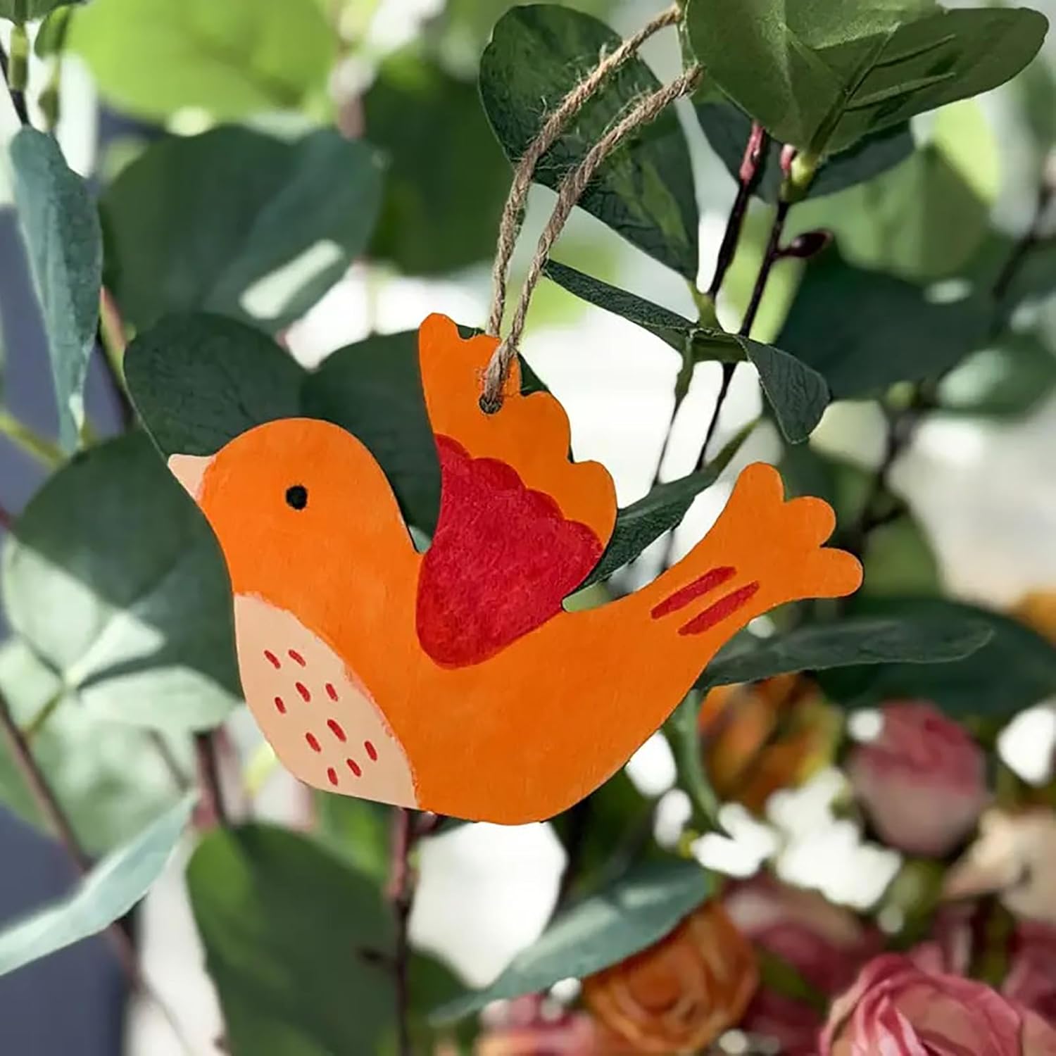 Decorative orange bird ornament with a red heart on a branch with leaves and flowers.