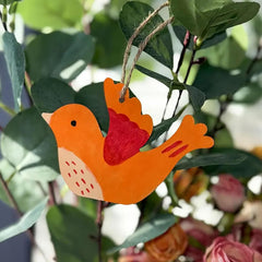 Decorative orange bird ornament with a red heart on a branch with leaves and flowers.