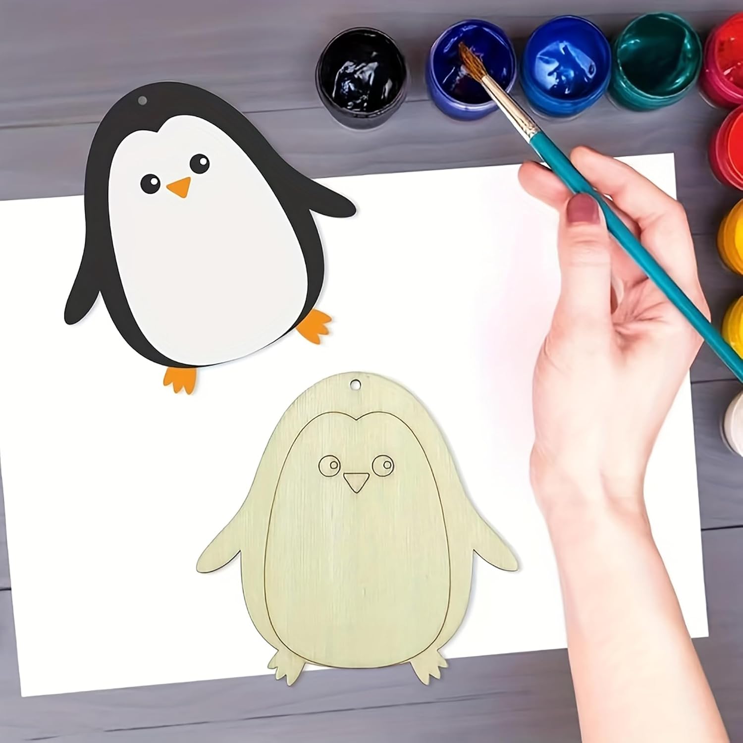Hand painting a cartoon penguin with watercolors on a white sheet of paper.