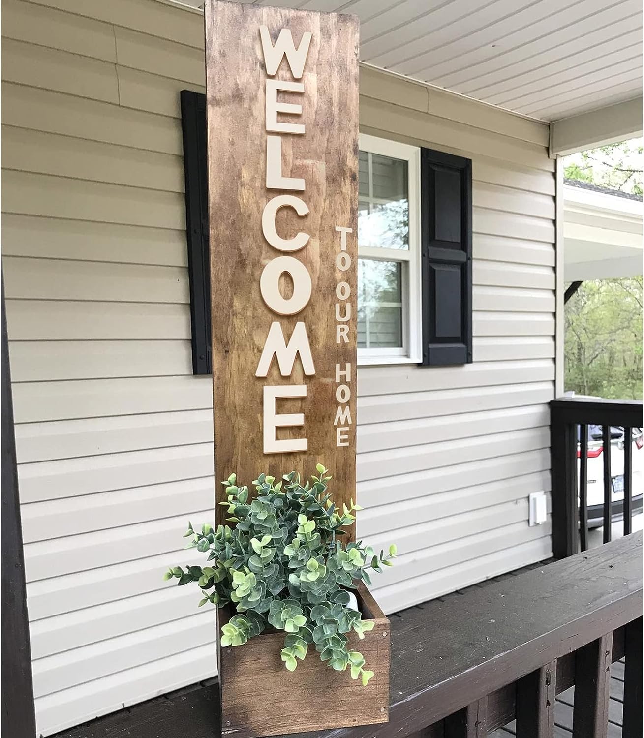 Wooden 'Welcome to our home' sign with plant holder on a porch.