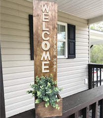 Wooden 'Welcome to our home' sign with plant holder on a porch.