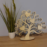Wooden tree decorative item with heart shapes on a wooden surface next to a plant.