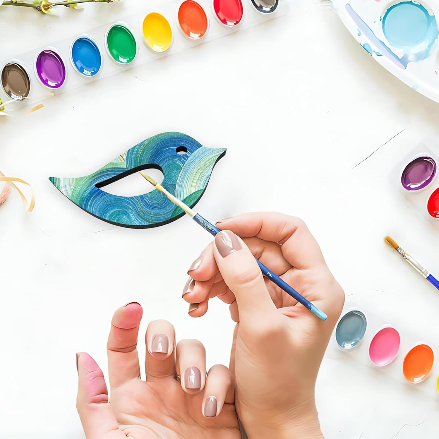 Person painting a ceramic fish with watercolors on a white surface