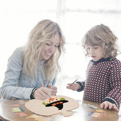 Woman and child painting a wooden board together on a light background
