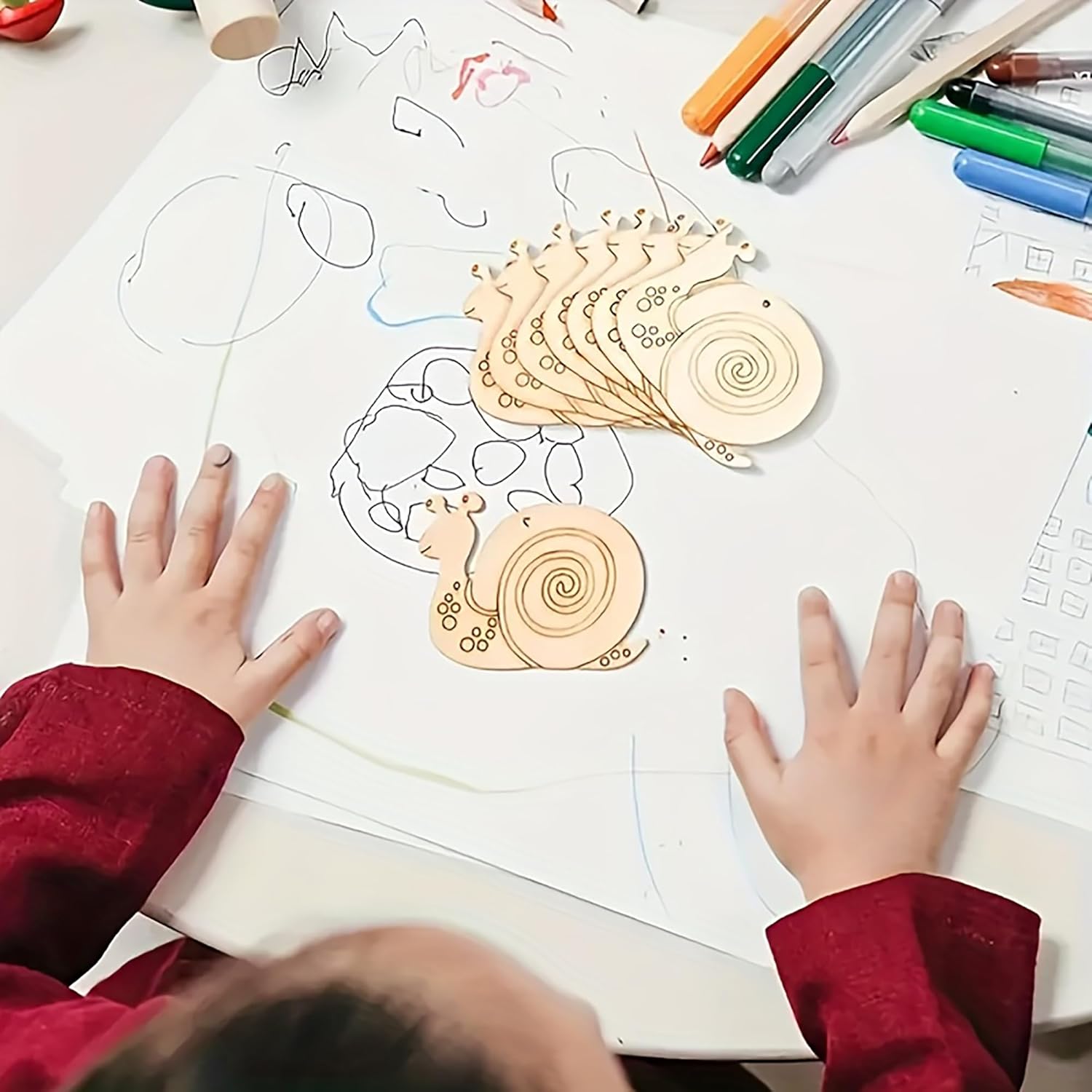 Children's hands tracing wooden snail templates on paper with colored markers.