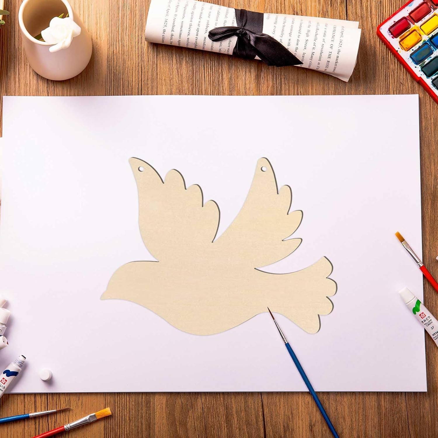 Paper cutout of a dove on a white sheet of paper with art supplies on a wooden table.