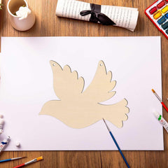 Paper cutout of a dove on a white sheet of paper with art supplies on a wooden table.