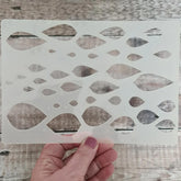 Hand holding a decorative stencil with leaf patterns on a wooden surface