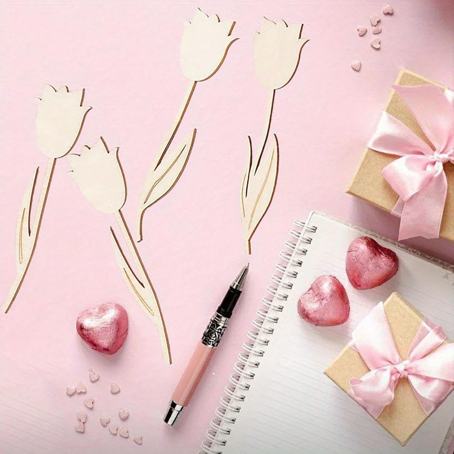 Pink tulips, heart-shaped candies, a pen, and small gift boxes on a pink background