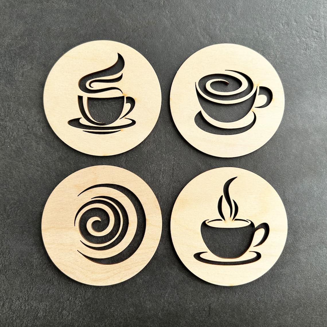Four wooden coasters with coffee cup designs on a dark surface
