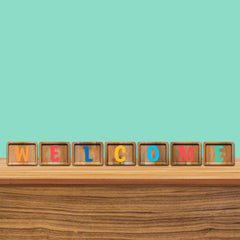 Wooden blocks with colorful letters spelling 'WELCOME' on a wooden surface with a teal background