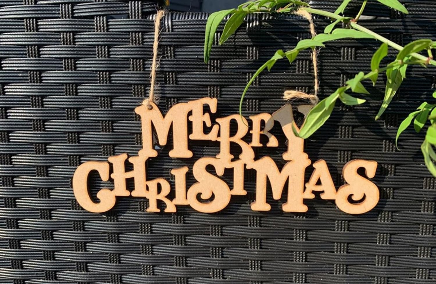 Wooden 'Merry Christmas' decoration hanging on a textured black surface with green leaves.