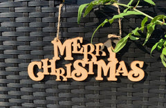 Wooden 'Merry Christmas' decoration hanging on a textured black surface with green leaves.