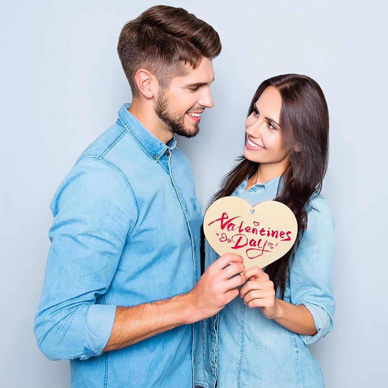 Man and woman holding a 'Valentine's Day' heart-shaped sign against a light blue background