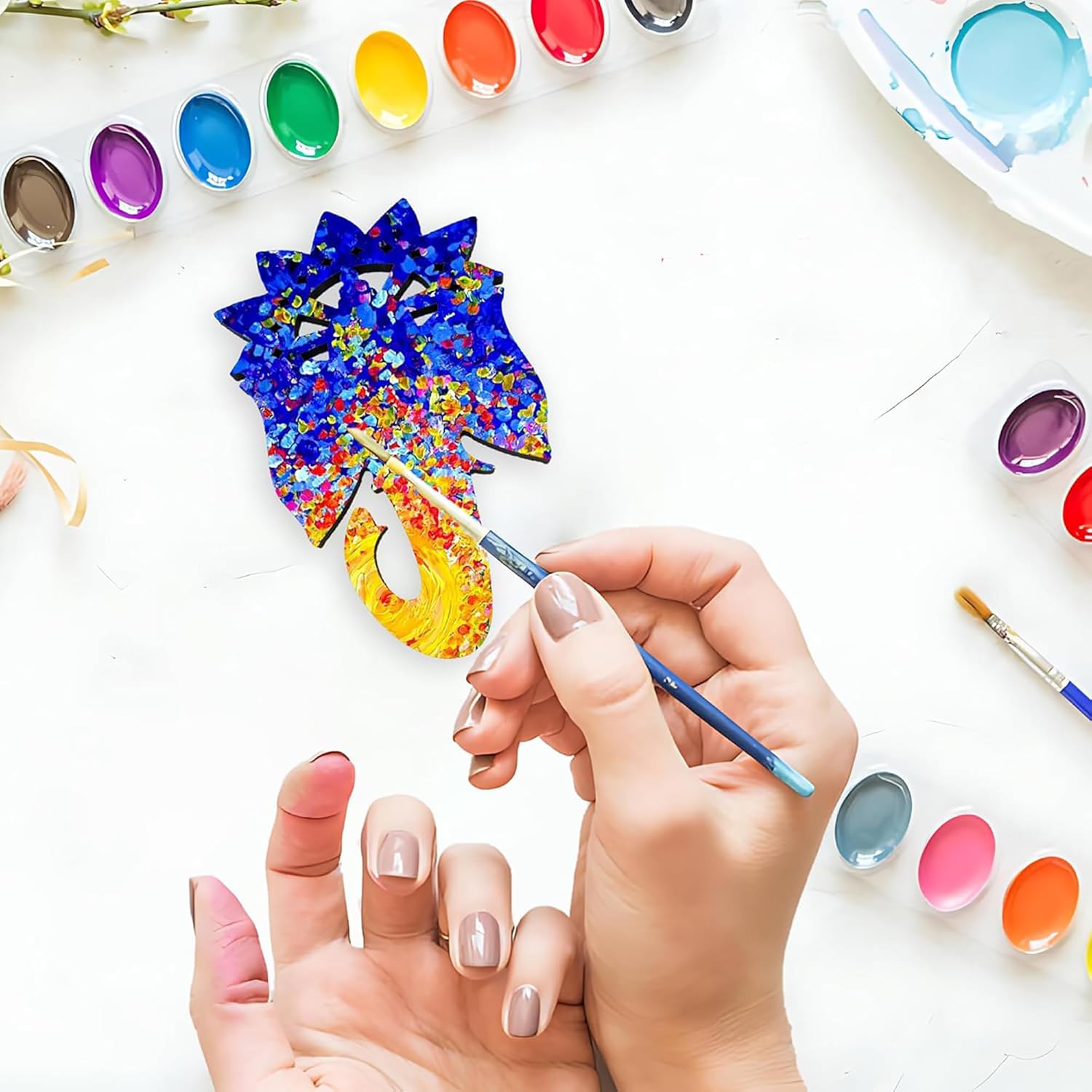 Person painting a colorful pine cone with watercolors on a white surface.