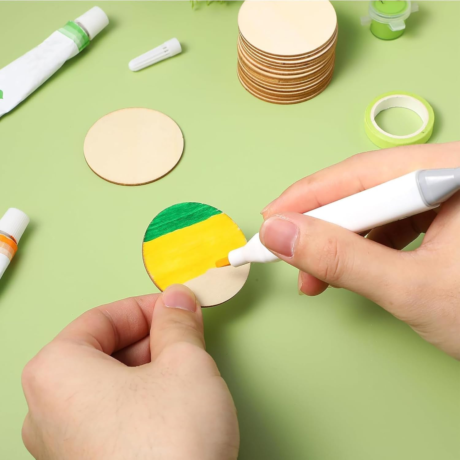 Person coloring a wooden circle with markers on a green surface