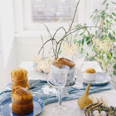 Decorative table setting with pastries, glasses, and butterfly lights on a light background.