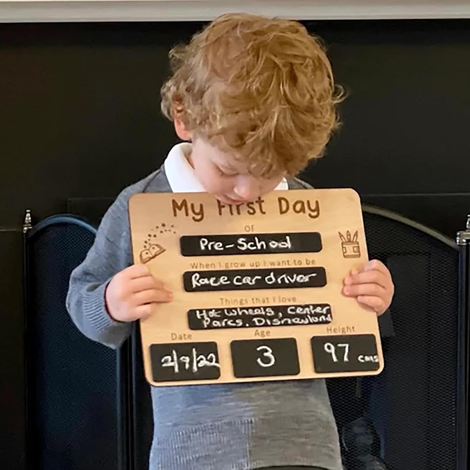 Child holding a 'My First Day of Pre-School' sign with handwritten text.