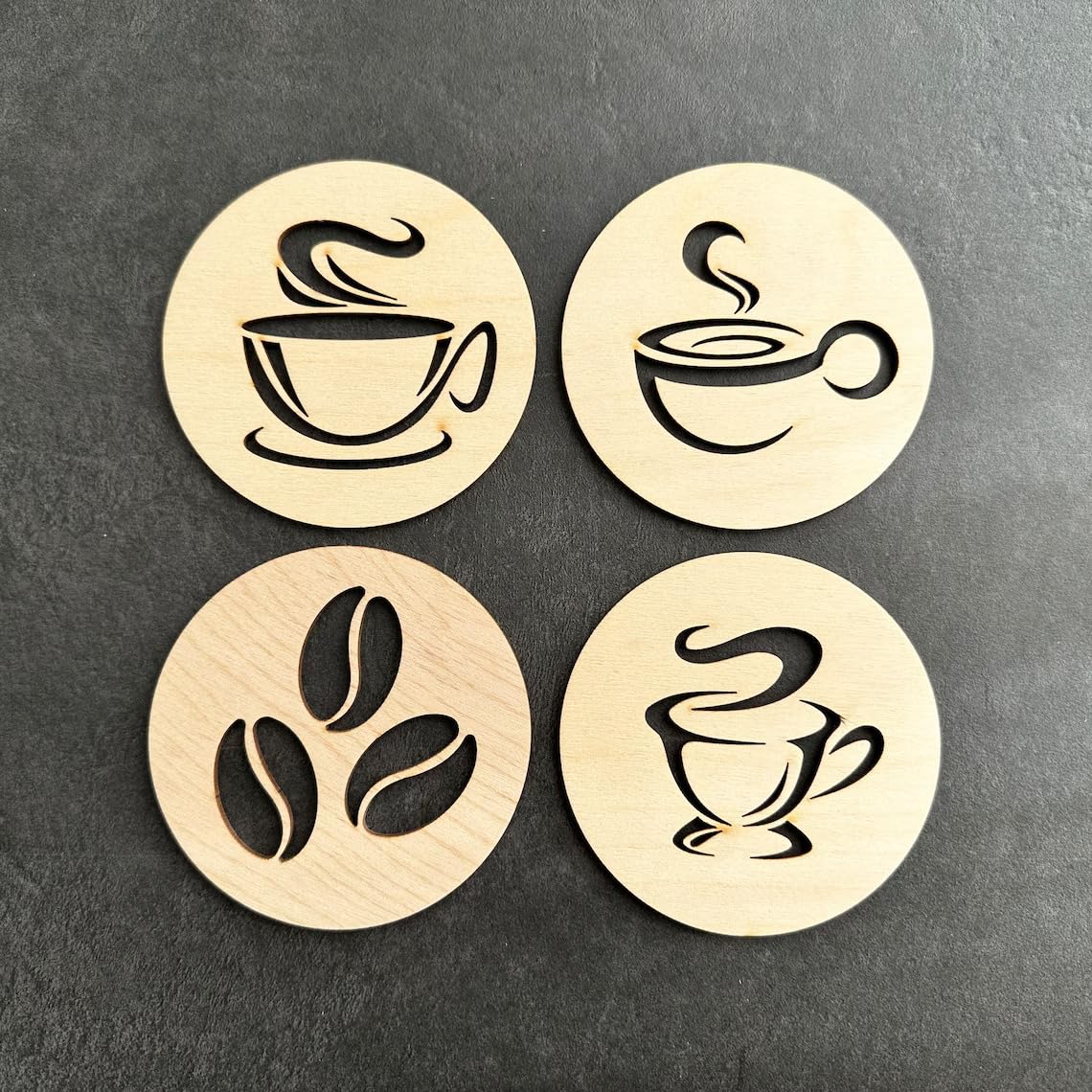 Four wooden coasters with coffee-themed designs on a dark surface
