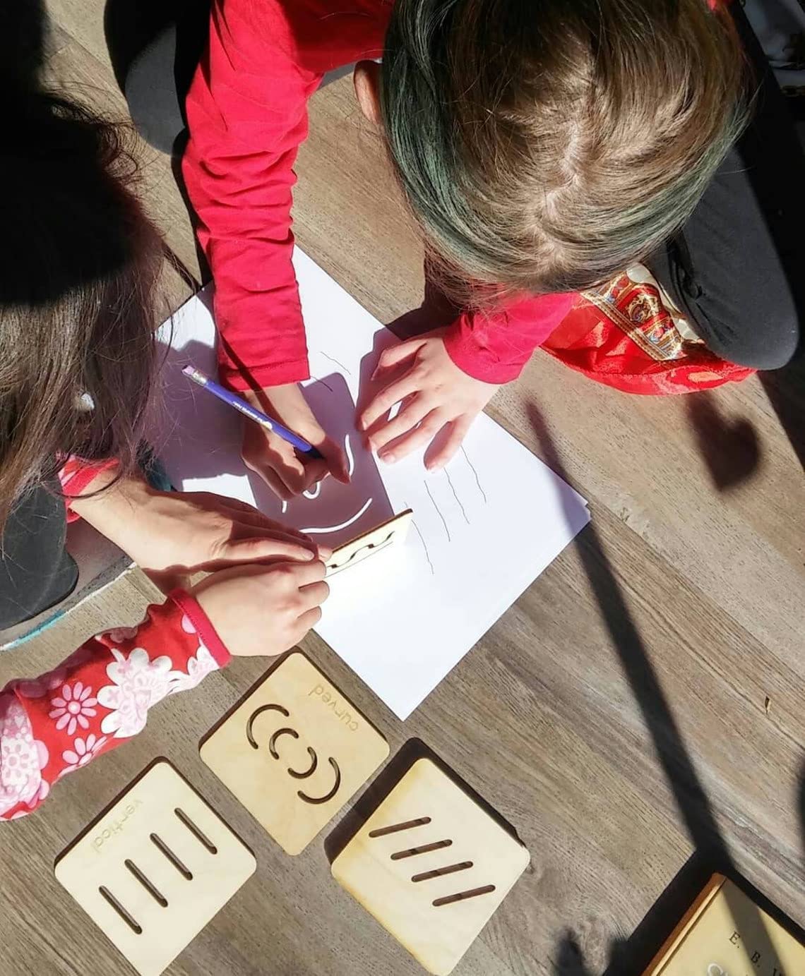 Two children drawing on paper with wooden stamps on a wooden table.