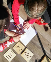 Two children drawing on paper with wooden stamps on a wooden table.