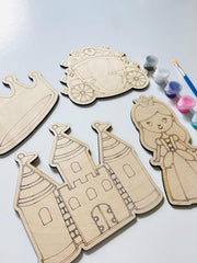 Wooden cutouts of a castle, crown, and princess on a light surface with paint supplies.