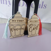 Two wooden ornaments with tassels, one saying 'My First Ramadan' and the other 'My First Eid', on a white surface.