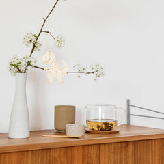 Tea set with a glass teapot, ceramic cups, and a vase on a wooden surface.