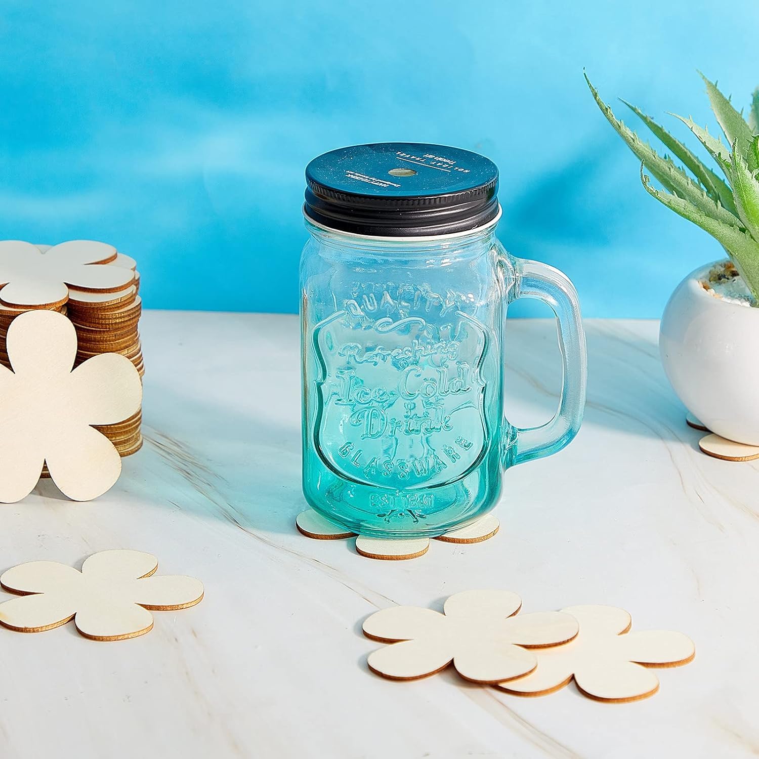 Clear glass jar with handle and black lid on a white surface with decorative items.