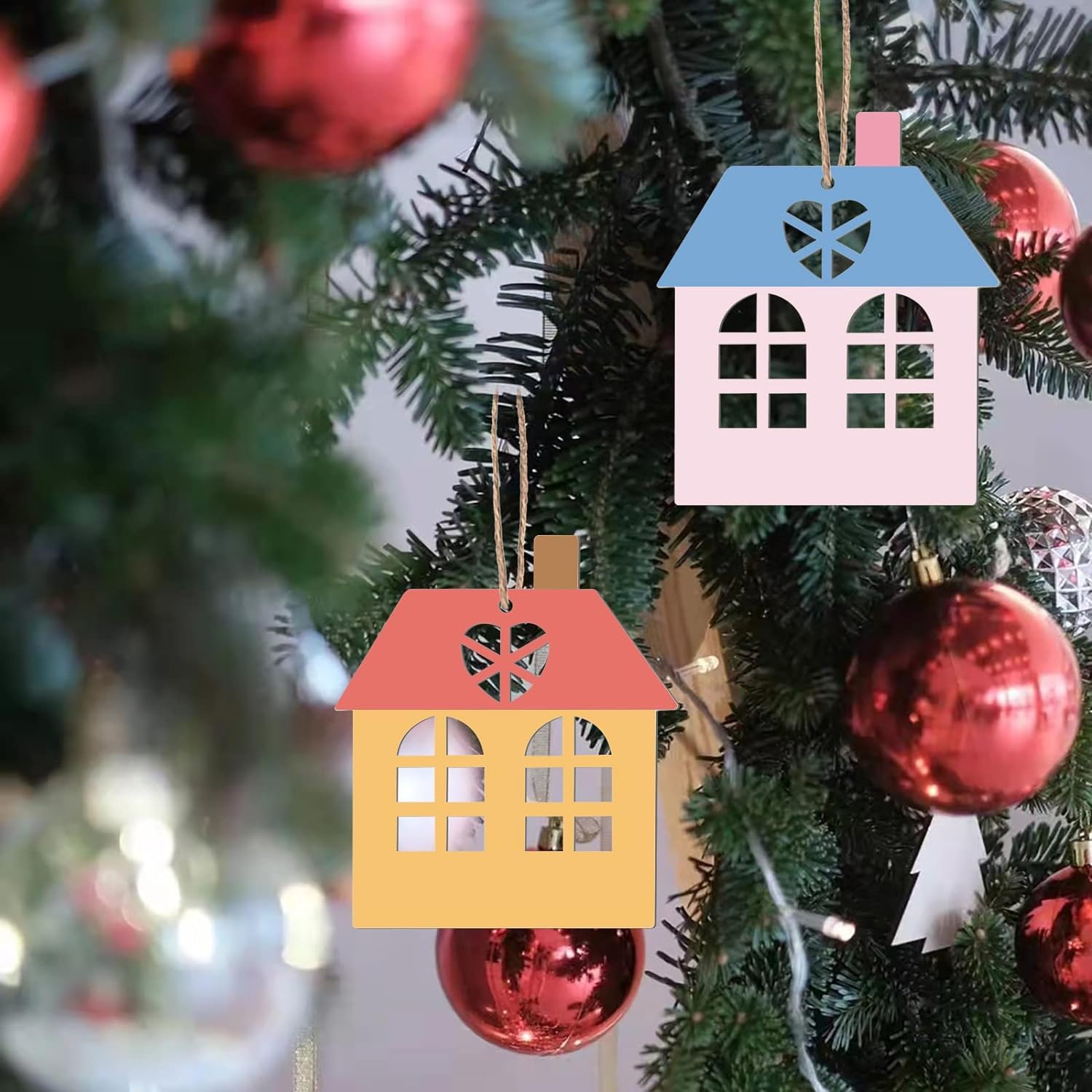 Colorful house-shaped ornaments on a Christmas tree with red baubles.