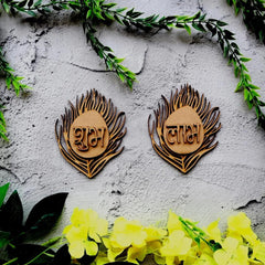 Wooden earrings with engraved text on a textured surface with greenery and flowers.