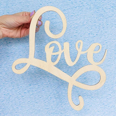 Wooden 'Love' decoration held by a hand against a blue background