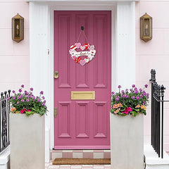 Pink front door with decorative heart wreath and flower pots on a white wall.